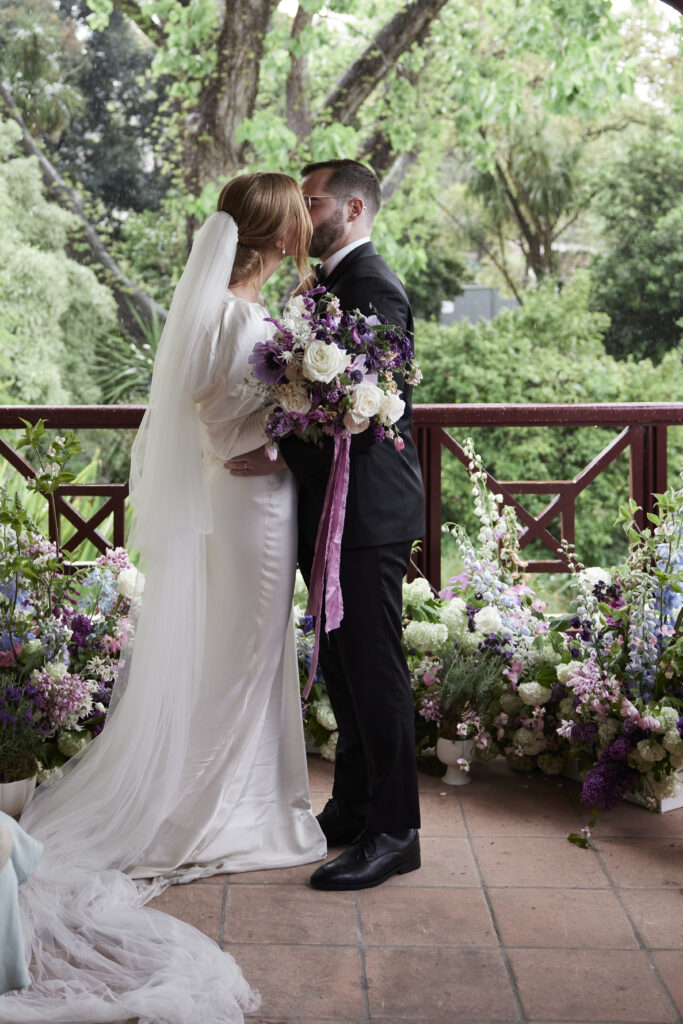 Bride and Groom in wedding outfits kissing in the centre surrounded by ceremony flowers