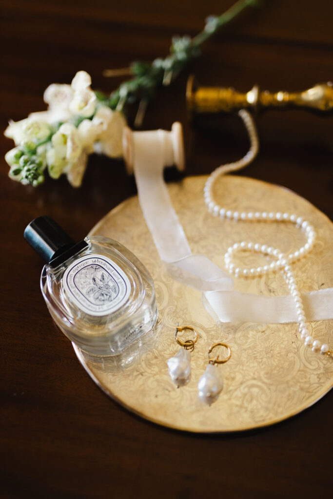 The image features a clock and a bottle of perfume by diptyque on a table.